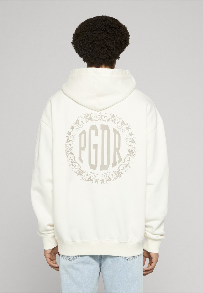 Sudadera blanca con capucha y un gran emblema floral beige que presenta el texto "PGDR" en la espalda. Cuenta con capucha con cordones y un ajuste holgado.
