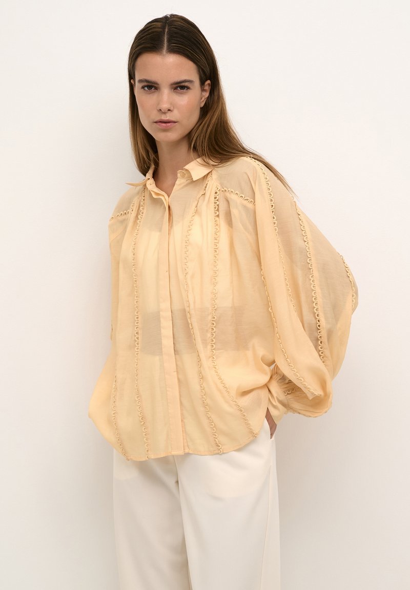 Helle gelbe, halbtransparente Bluse mit durchgängiger Knopfleiste, voluminösen Ärmeln und dekorativen gestickten Details entlang der Nähte.