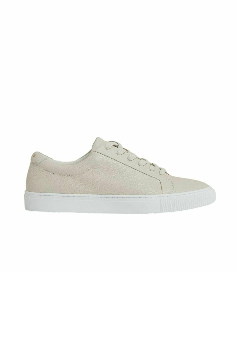 Adidași din piele bej cu suprafață texturată, talpă albă, vârf rotund și șase găuri pentru sireturi, având un design minimalist.