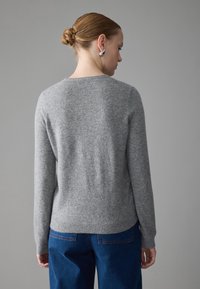 Gray knitted sweater with a round neckline and long sleeves, made of soft material, paired with blue high-waisted pants.