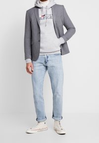 Blazer de rayas grises sobre una sudadera gris con logo, combinado con jeans de color azul claro y zapatillas altas crema.