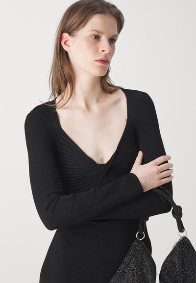 Μαύρο μακρυμάνικο εφαρμοστό φόρεμα με βαθύ V-λαιμό και ριγέ υφή στην κορυφή. Διακοσμημένο με μια μαύρη κωδική τσάντα με λάμψη.