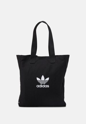 Sac cabas noir Adidas avec doubles poignées et logo trefoil blanc centré à l'avant sur un fond gris clair uni.