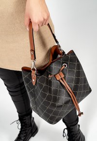 Borsa a secchiello nera con un motivo trapuntato e dettagli in pelle color cuoio, dotata di chiusura con coulisse e tracolla regolabile.