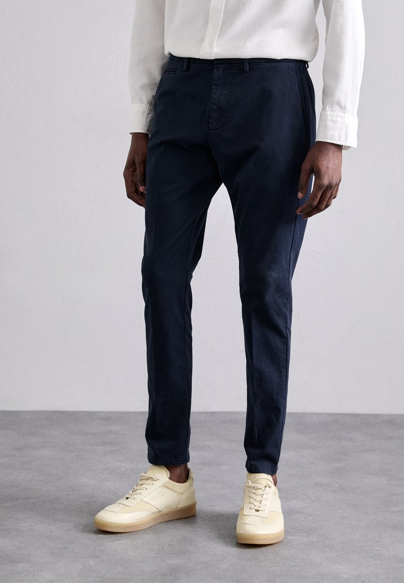 Chinos navy hechos de una tela suave, con corte ajustado y bolsillos laterales, combinados con zapatillas de color amarillo claro con una suela texturizada.