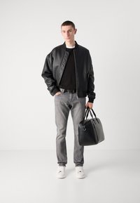 Chaqueta bomber de cuero sintético negra, jeans grises, zapatillas blancas y un bolso estructurado negro con doble asa, todo sobre un fondo liso.