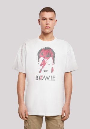 White cotton t-shirt featuring a graphic of a face with red and gray hair, lightning bolt, and "BOWIE" text in black below the image.