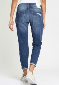 Jeans i denim med medelhög midja, mörkblå färg, uppvikta fållar, två bakfickor och en liten detalj på midjebandet.