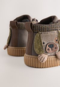 Braune Stiefeletten mit Cord-Akzenten und einem Hundegesichts-Design. Gewebe mit Struktur, Gummisohle und Schlaufen an der Rückseite für einfaches An- und Ausziehen.