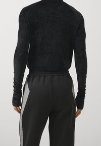 Maglia nera a maniche lunghe realizzata in tessuto morbido, abbinata a pantaloni sportivi neri con pannelli laterali grigi e vita elastica.