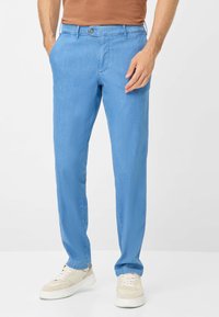 Pantaloni azzurri chiari in una vestibilità rilassata, realizzati in un tessuto morbido. Presentano tasche inclinate, una chiusura a bottone e sono abbinati a sneaker bianche.