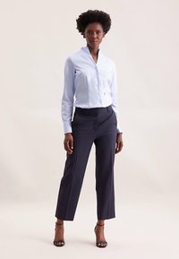 Camicia a righe azzurro chiaro con bottoni e collo alla coreana, abbinata a pantaloni a vita alta blu scuro e sandali neri con tacco.