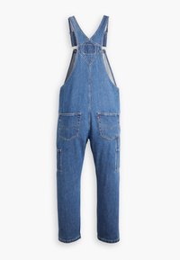Salopette en denim bleu avec bretelles réglables, poches avant et arrière, et coupe décontractée. Présente un design classique et une texture de tissu robuste.