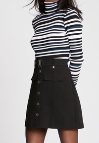 Zwarte A-lijn rok met een sluiting aan de voorkant, twee zakken en een ceintuur in de taille. Gestreepte coltrui in zwart, wit en blauw.