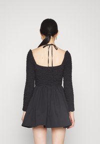 Svart klänning med en texturerad, rynkad bodice, långärmar och en utsvängd kjol. Baksidan har en öppen design med en knytning.