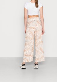 White crop top paired with wide-leg pants featuring a beige and white leaf pattern. Pants have an elastic waistband and pockets.