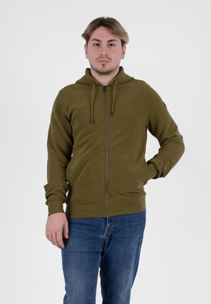 Felpa con zip color verde oliva, dalla finitura texture, con cappuccio regolabile tramite cordino, polsini e vita a coste, abbinata a jeans blu.