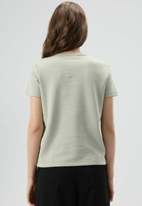 Lichtgroen T-shirt met korte mouwen en een ronde hals. Zachte stof, smalle pasvorm en een gladde textuur. Achteraanzicht toont minimale naden en stiksels.