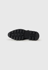 Suola di scarpa in gomma nera con motivo di battistrada testurizzato, caratterizzata da profonde scanalature e una sezione della punta arrotondata. Design resistente per una buona trazione.