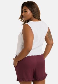 Débardeur blanc sans manches avec une finition texturée, associé à un short bordeaux avec un ourlet à volants et des poches latérales.
