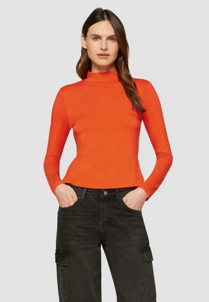 Langsleeve, aansluitend coltrui in feloranje, gemaakt van een glad materiaal, gecombineerd met donkere cargobroek met zijzakken.