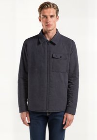 Marineblå quiltet jakke med lynlås foran, spredt krave og en brystlomme med trykknapdetalje. Glat tekstur og tætsiddende design.
