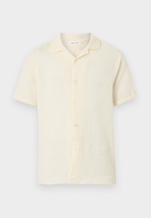 Chemise texturée à manches courtes de couleur crème, à boutons, avec un col camp, présentée sur un fond blanc.