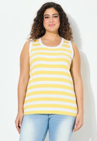 Gul och vit randig linne med rundad halsringning och ärmlös design, tillverkad av ett texturerat tyg. Kombinerad med ljusblå jeans.