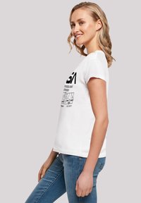 White cotton t-shirt featuring black text and graphics on the front. Short sleeves, round neckline, and a relaxed fit. Blue jeans are worn.
