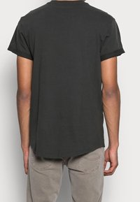 Czarna bawełniana koszulka z krótkimi rolowanymi rękawami, zaokrąglonym dołem i luźnym krojem. Gładka faktura, brak widocznych wzorów czy dodatków.