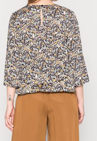 Blusa a fantasia floreale di colore blu scuro, con fiori gialli e azzurri, maniche a tre quarti e chiusura con bottone a chiave sul retro.