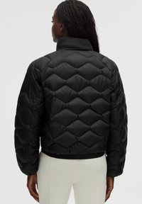 Chaqueta de plumas negra con un diseño de acolchado en cuadros, cuello alto y dobladillo elástico. Presenta un acabado suave y brillante, así como una silueta voluminosa.