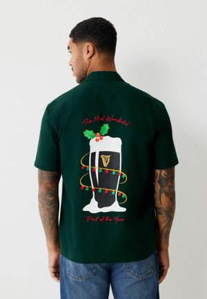 Green short-sleeve shirt featuring a festive Guinness pint graphic, colorful decorations, and text "The Most Wonderful Part of the Year."