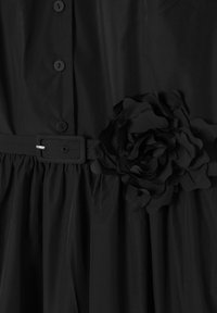 Čierne šaty so zapínaním na gombíky, plisovanou sukňou a látkovým kvetinovým ozdobením na páse, vyrobené z hladkého materiálu.