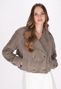 Giacca corta doppiopetto in suede taupe con grandi bottoni, colletto a punta e tasche laterali. Texture liscia con vestibilità rilassata.