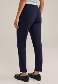 Námořnické modré kalhoty s hladkou texturou, mají zúžený střih a dvě zadní kapsy. V kombinaci s černými botami pro elegantní vzhled.