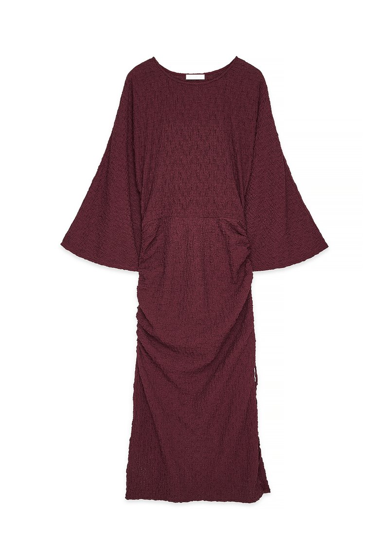 Burgundy, strukturoitu mekko leveillä hihoilla, pyöreällä kaula-aukolla ja rypytetyillä yksityiskohdilla vyötäröllä, ulottuen polven puoliväliin.