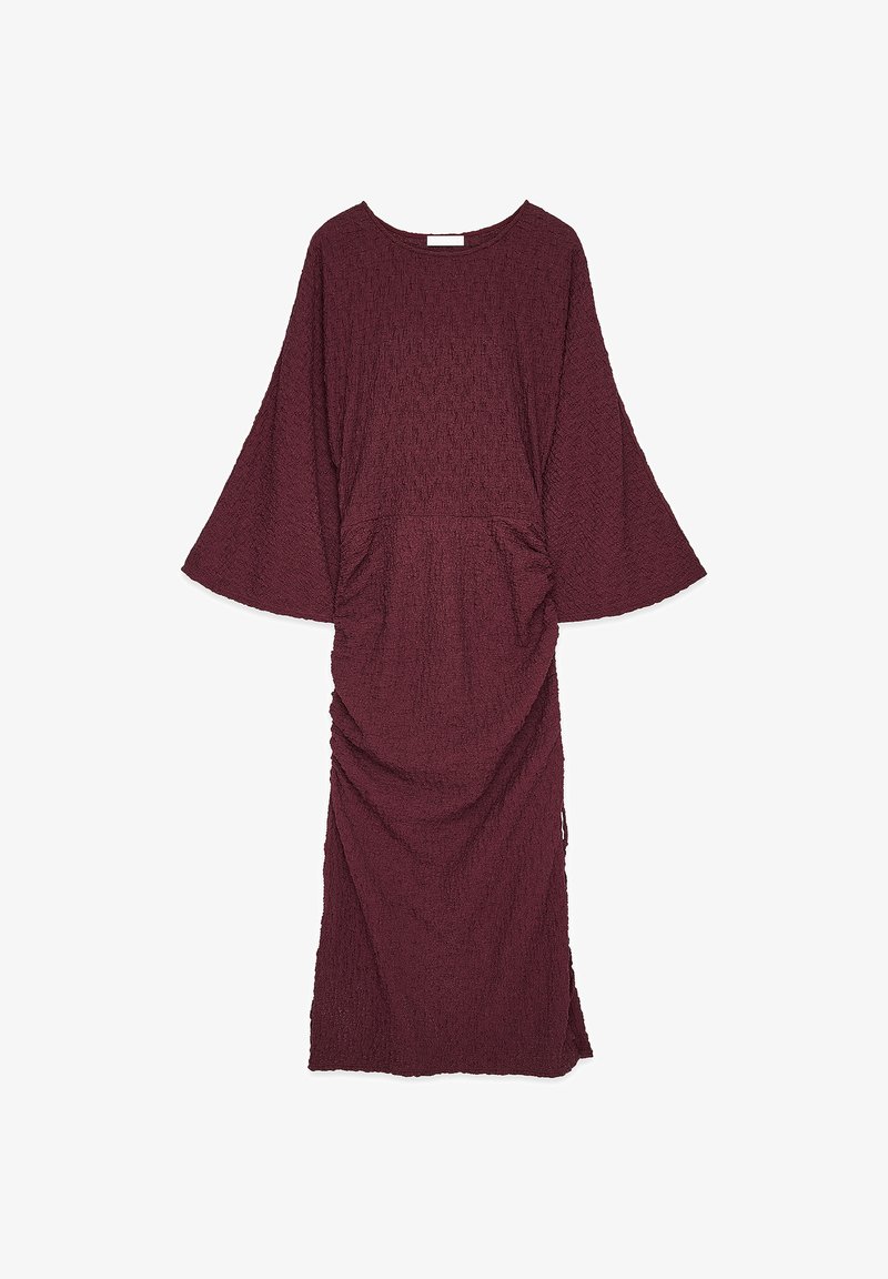 Bordowa sukienka o fakturowanej tkaninie, z szerokimi rękawami, okrągłym dekoltem i marszczeniem w talii, sięgająca do połowy łydki.