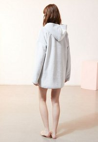 Light gray oversized hoodie made of soft fabric, featuring a hood and long sleeves, displayed from the back on a bare floor.