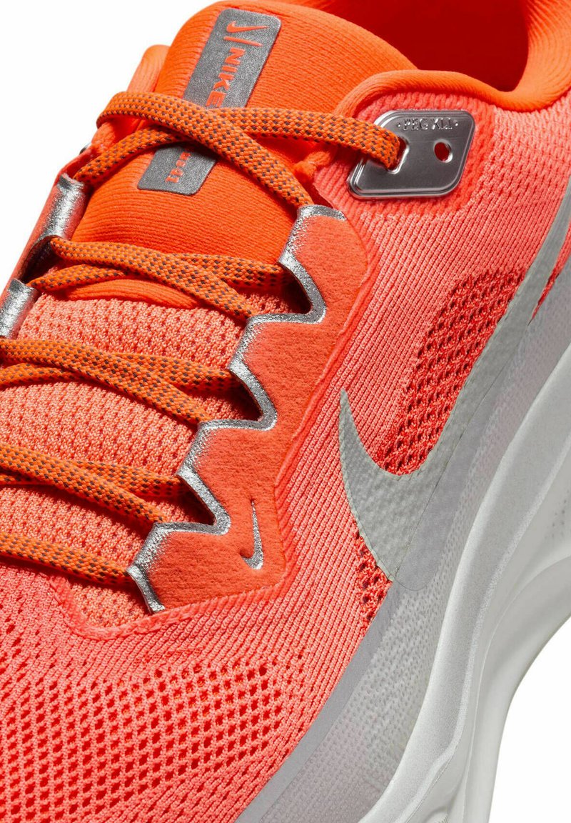 Botte de sport orange vif avec une tige en maille texturée, des accents argentés et un système de laçage distinctif. Caractéristiques d'une semelle blanche avec un détail de logo.