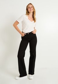 Pantalones vaqueros negros acampanados con cintura alta y bolsillos delanteros, combinados con una camiseta de manga corta de pico blanca y zapatillas blancas.