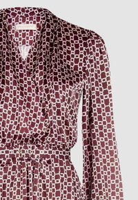 Abito color amaranto con motivo a catena bianca, realizzato in tessuto liscio. Presenta una scollatura a V e una cintura elastica in vita, con maniche lunghe.