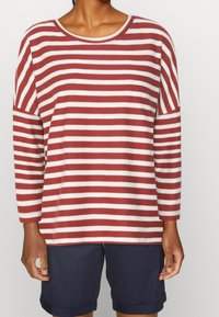 Maglia a maniche lunghe a righe rosse e bianche con collo a barca e vestibilità comoda, abbinata a pantaloni corti scuri. Il tessuto sembra morbido e leggero.
