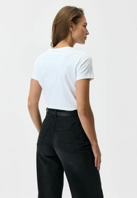 Biała bawełniana koszulka z krótkim rękawem, w zestawieniu z czarnymi, wysokim stanem spodniami dżinsowymi o gładkiej fakturze i dwoma kieszeniami z tyłu.