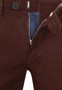Braune Baumwollhose mit Reißverschluss und kontrastierendem Innenfutter. Mit Knopfverschluss und silbernem Reißverschluss mit genähten Details.