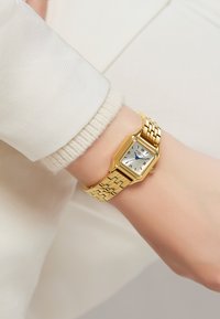 Montre rectangulaire dorée avec un cadran argenté, des chiffres romains noirs et des aiguilles bleues. Dispose d'un bracelet en maillons avec une finition polie.