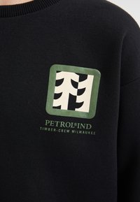 Sweat-shirt noir avec un logo bordé de vert représentant des arbres stylisés et le texte "PETROLIND TIMBER-CREW MILWAUKEE" en vert.