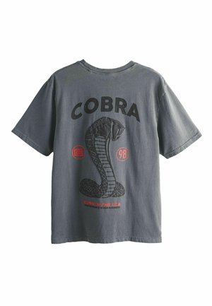 Tumehall shirt musta groter musta kobragraafika ja tekstiga "COBRA" ülalt, punaste aktsentidega, sealhulgas tekstiga "Born in the USA" all.