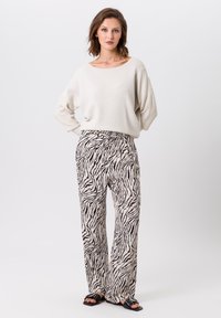 Lichtcrème oversized gebreide trui gecombineerd met loszittende, zebra-gestreepte broeken met een trekkoord en wijde pijpen. Zwarte sandalen.