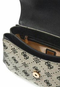 Sac à main structuré en tissu beige avec motif logo noir. Garniture en cuir noir et fermeture à pression dorée. L'intérieur révèle une doublure foncée et une poche zippée.